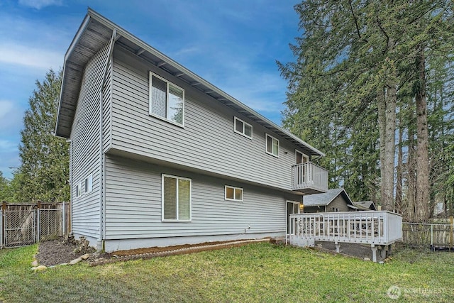 rear view of house with a deck, a balcony, a yard, and fence