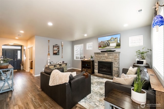 living room featuring visible vents, arched walkways, dark wood-type flooring, a stone fireplace, and recessed lighting