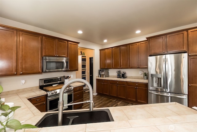 kitchen featuring tile countertops, dark wood-style flooring, stainless steel appliances, a sink, and recessed lighting