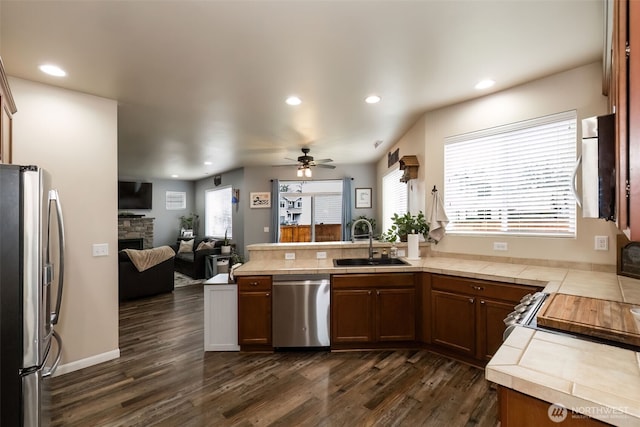 kitchen with a stone fireplace, stainless steel appliances, a peninsula, a sink, and open floor plan