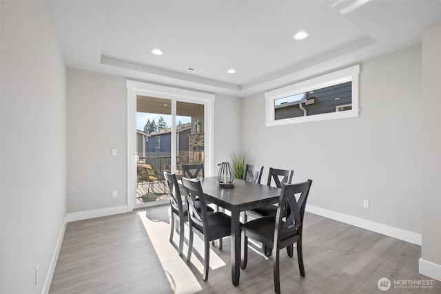 dining area featuring baseboards, a raised ceiling, and wood finished floors