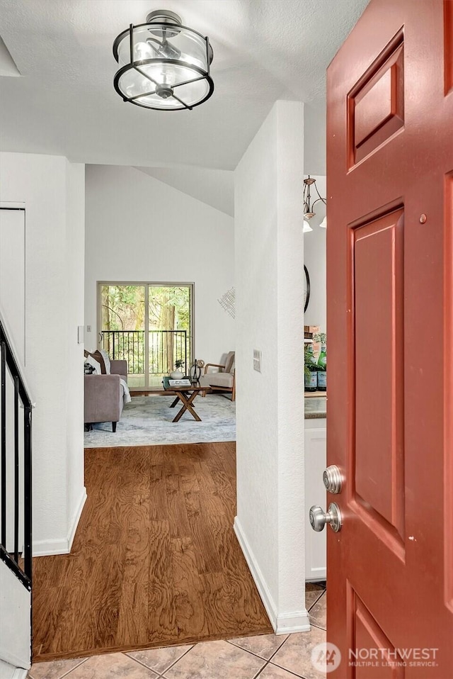 foyer featuring light wood finished floors, stairs, baseboards, and vaulted ceiling