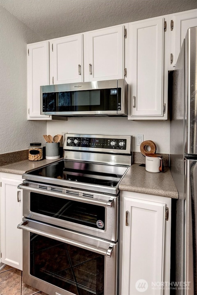 kitchen with a textured wall, stainless steel appliances, and white cabinets