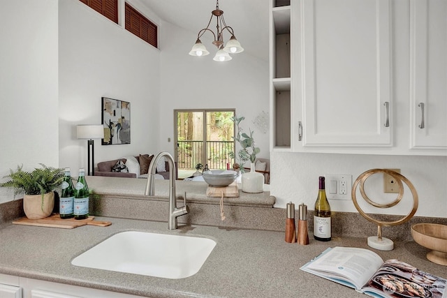 kitchen with a high ceiling, a sink, white cabinets, an inviting chandelier, and pendant lighting