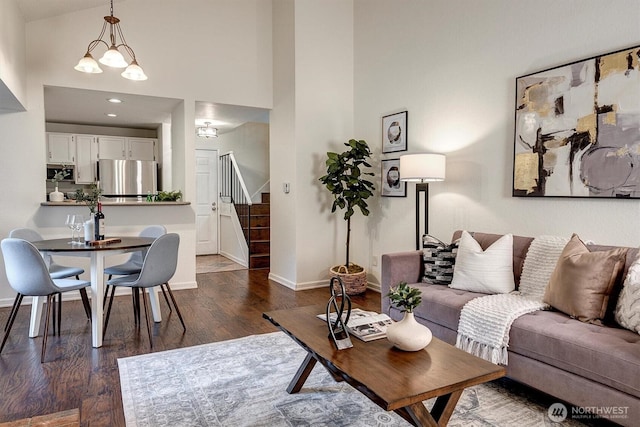 living area featuring baseboards, dark wood-style floors, a high ceiling, stairs, and a chandelier