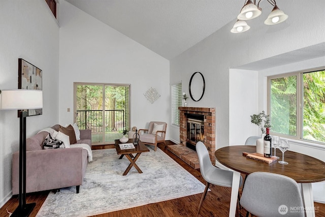 living area with a brick fireplace, high vaulted ceiling, wood finished floors, and an inviting chandelier