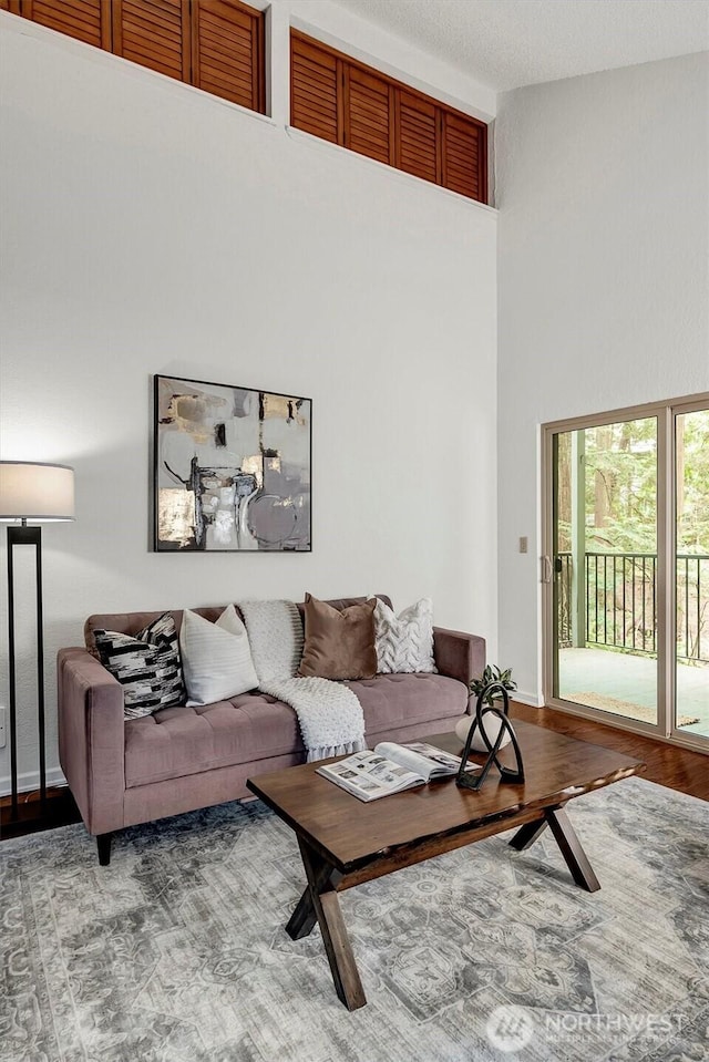 living area featuring wood finished floors, a towering ceiling, and baseboards