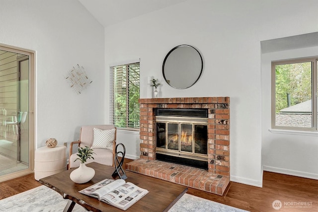 living room with lofted ceiling, a brick fireplace, wood finished floors, and baseboards