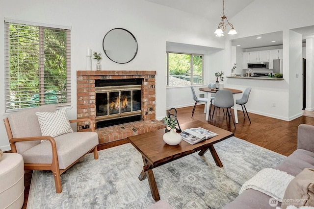 living room featuring high vaulted ceiling, a notable chandelier, a fireplace, wood finished floors, and baseboards