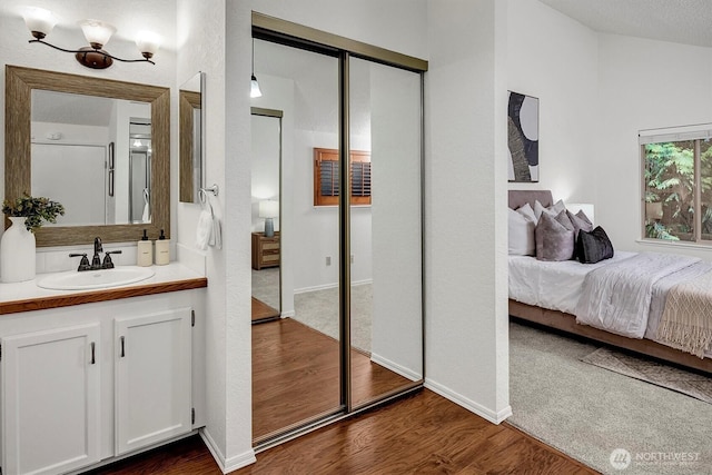 bedroom featuring dark wood-style floors, a closet, a sink, vaulted ceiling, and baseboards