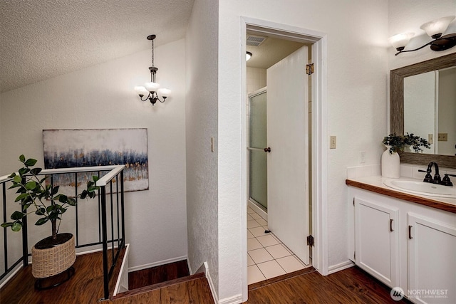 bathroom with a stall shower, wood finished floors, vaulted ceiling, a textured ceiling, and vanity