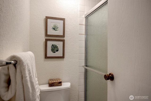 bathroom featuring toilet, a textured wall, and a shower with shower door