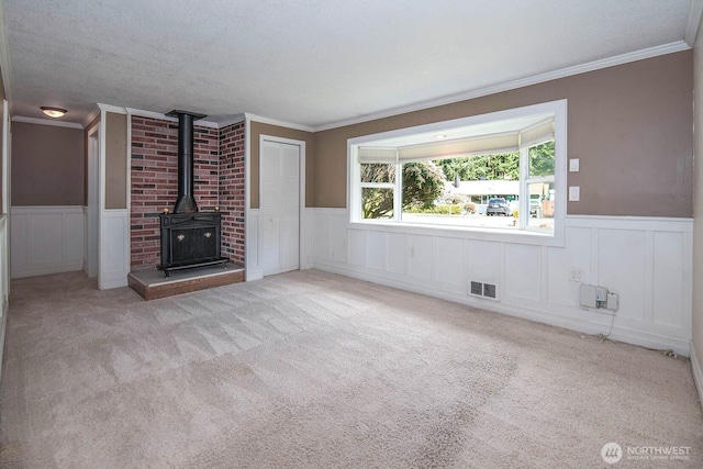 unfurnished living room featuring a wood stove, a wainscoted wall, visible vents, and carpet flooring