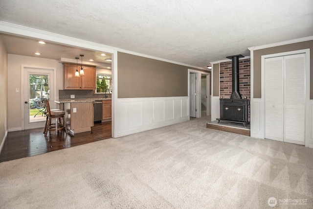 unfurnished living room with wainscoting, carpet, and a wood stove