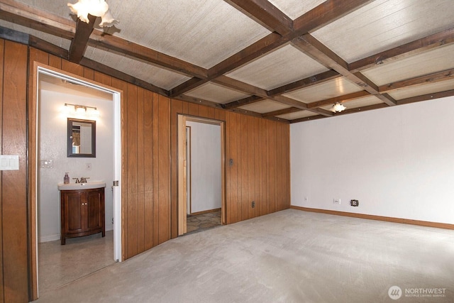 unfurnished bedroom featuring baseboards, coffered ceiling, beamed ceiling, wood walls, and a sink