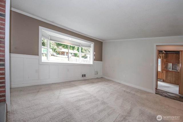 carpeted spare room featuring a baseboard radiator, visible vents, crown molding, and wainscoting