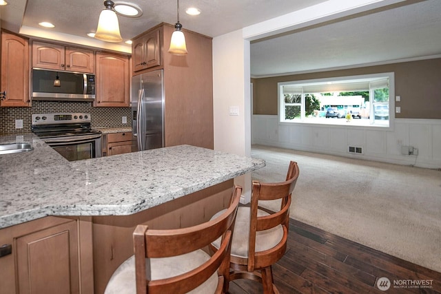 kitchen with light stone counters, appliances with stainless steel finishes, wainscoting, and visible vents