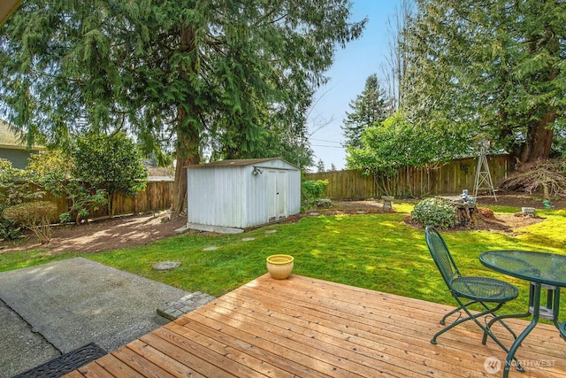 wooden deck featuring a yard, a fenced backyard, a storage unit, and an outbuilding