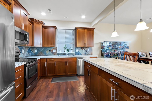 kitchen featuring visible vents, dark wood-type flooring, decorative light fixtures, stainless steel appliances, and a sink