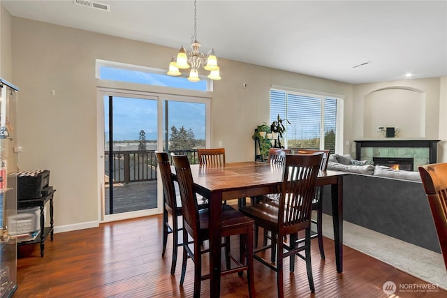 dining room featuring a tile fireplace, a notable chandelier, dark wood-type flooring, visible vents, and baseboards