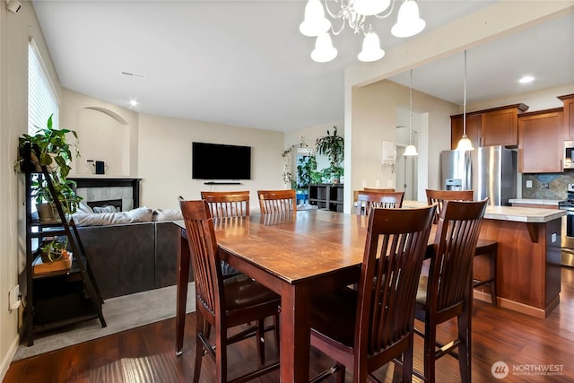 dining space featuring dark wood-type flooring, a fireplace, and an inviting chandelier