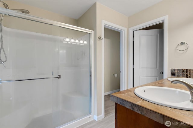 full bath with a sink, a shower stall, baseboards, and wood finished floors