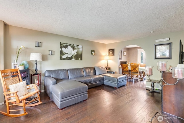 living room featuring dark wood-type flooring, baseboards, arched walkways, and a textured ceiling