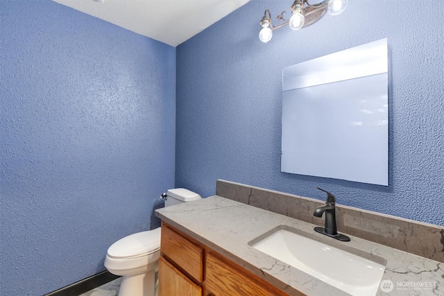 bathroom with vanity, toilet, and a textured wall