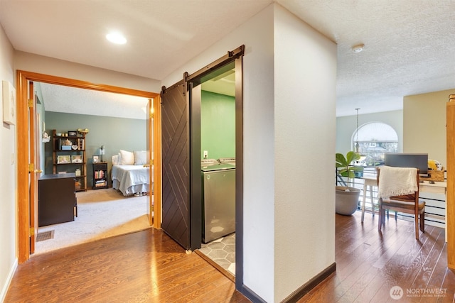 corridor with washer and dryer, a textured ceiling, a barn door, and wood-type flooring