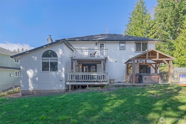 back of property featuring a balcony, a lawn, fence, and a hot tub