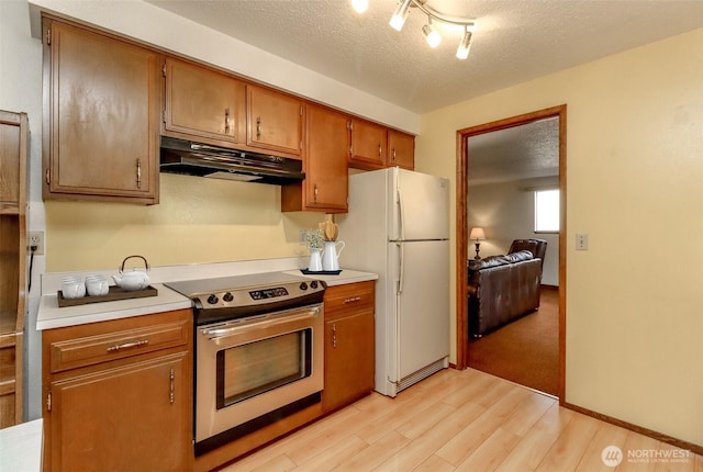 kitchen with stainless steel electric range oven, light countertops, freestanding refrigerator, a textured ceiling, and under cabinet range hood