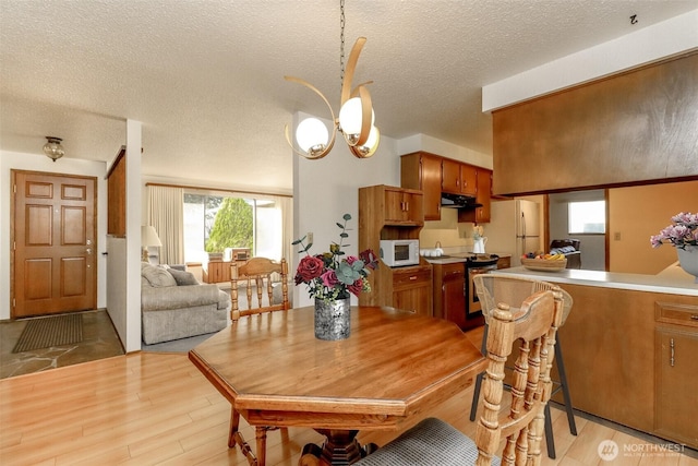 dining area with light wood-style flooring, a textured ceiling, and a notable chandelier