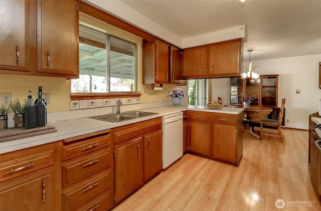 kitchen with dishwasher, brown cabinets, a peninsula, light countertops, and a sink