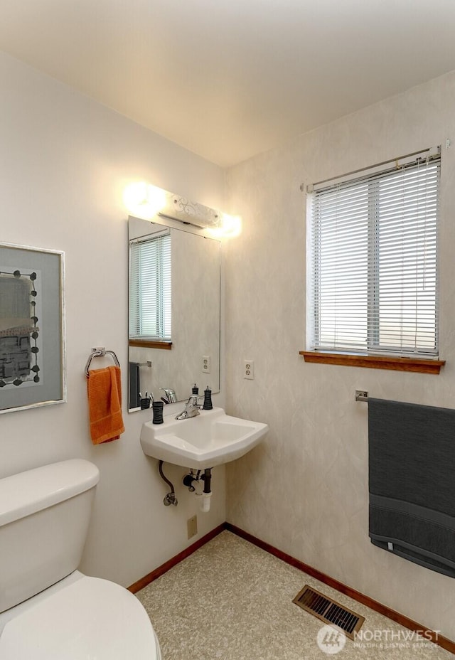 half bathroom with heating unit, visible vents, toilet, a sink, and baseboards