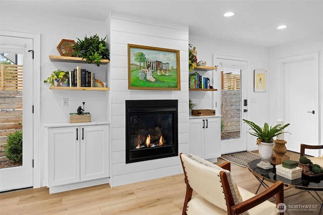 living area featuring light wood-style floors, a glass covered fireplace, and recessed lighting