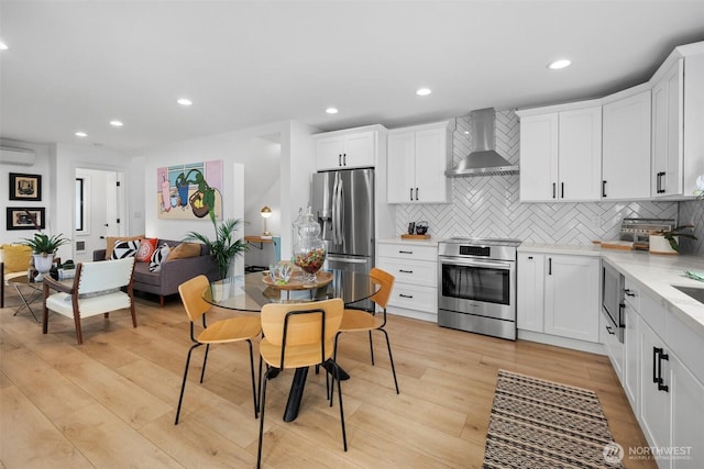 kitchen featuring decorative backsplash, light wood-style floors, appliances with stainless steel finishes, wall chimney range hood, and recessed lighting