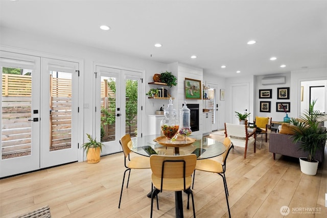 dining area with french doors, a fireplace, recessed lighting, an AC wall unit, and light wood-type flooring