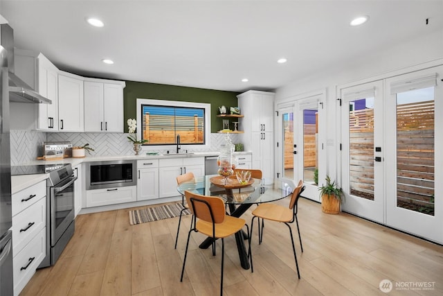 kitchen featuring french doors, stainless steel appliances, light countertops, wall chimney range hood, and light wood-type flooring