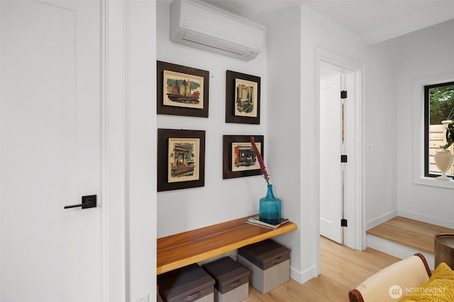 hallway with a wall mounted AC, light wood-style flooring, and baseboards