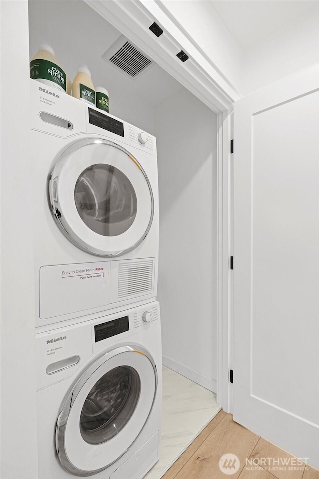 clothes washing area with baseboards, laundry area, visible vents, and stacked washer / drying machine