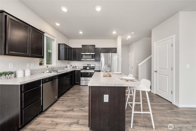 kitchen with light wood-type flooring, appliances with stainless steel finishes, a breakfast bar, and light countertops