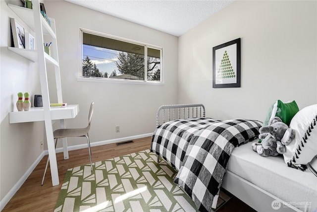 bedroom featuring visible vents, a textured ceiling, baseboards, and wood finished floors