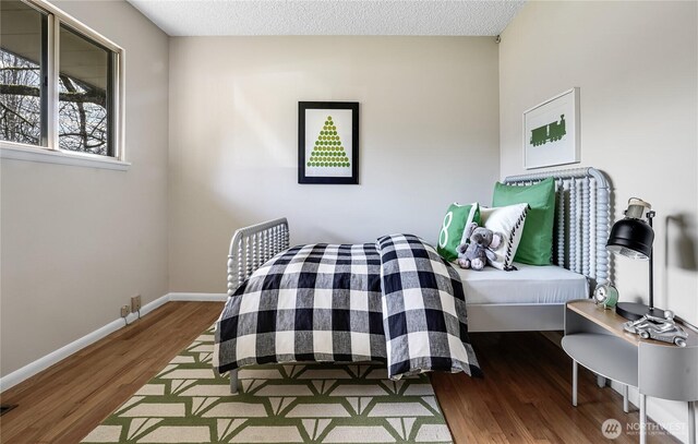 bedroom featuring visible vents, a textured ceiling, baseboards, and wood finished floors