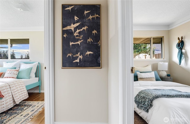 bedroom featuring baseboards, a textured ceiling, wood finished floors, and ornamental molding