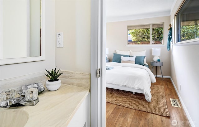 bedroom featuring visible vents, baseboards, wood finished floors, and crown molding