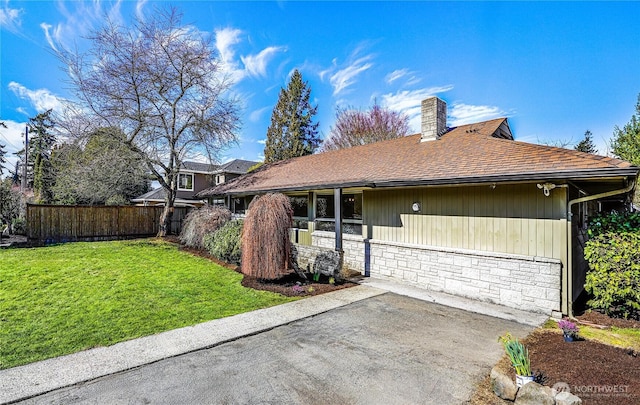 view of front facade featuring a front yard, fence, a shingled roof, a chimney, and stone siding