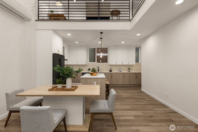 dining room featuring a wall mounted AC, wood finished floors, a towering ceiling, and baseboards