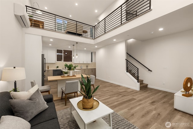 living room with baseboards, light wood-style flooring, a high ceiling, and a wall mounted AC