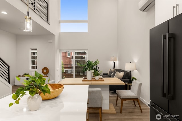 dining area with a wall unit AC, a high ceiling, light wood-type flooring, baseboards, and stairs