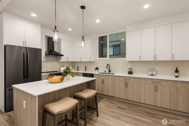 kitchen featuring wall chimney exhaust hood, freestanding refrigerator, light wood-style floors, a kitchen bar, and a sink